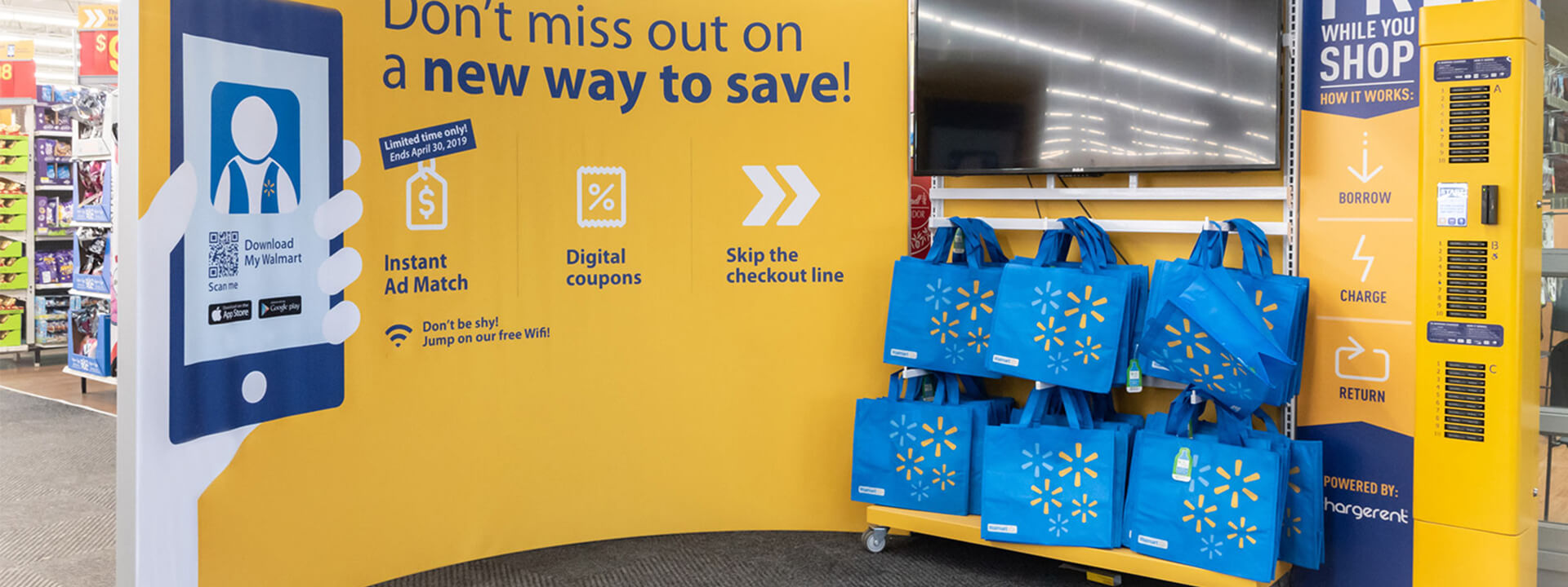 A Walmart store display advertises the My Walmart app features, reusable shopping bags, and a hargerent phone charging station.