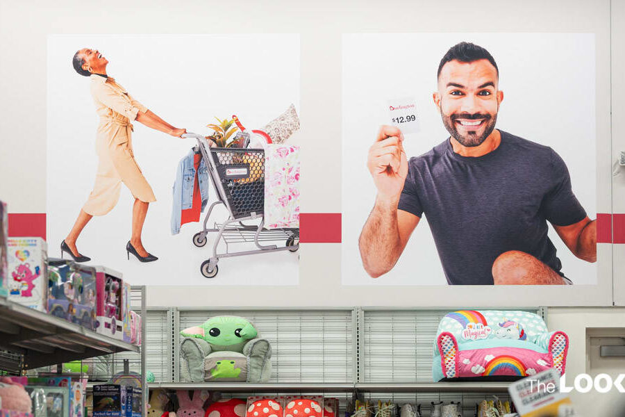 Large in-store displays feature a joyful woman pushing a shopping cart and a smiling man holding a ""Burlington $12.99"" card, above retail shelves.
