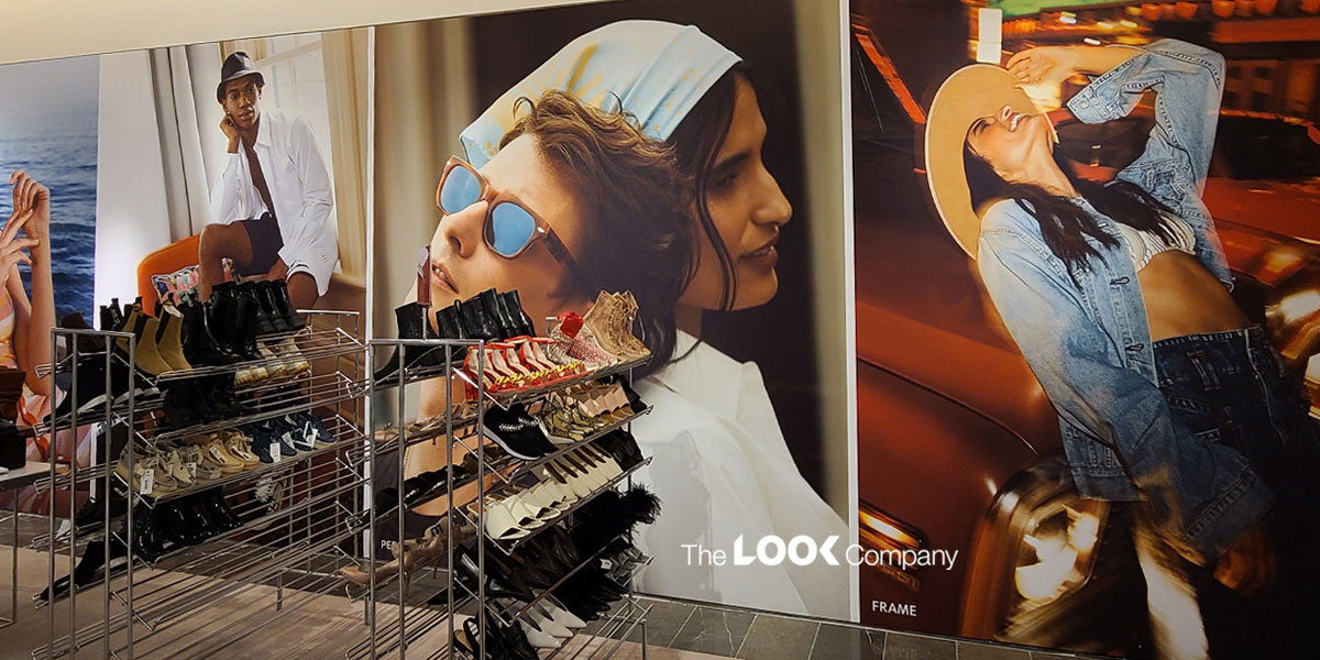Metal shoe racks displaying various footwear are positioned in front of large wall advertisements featuring fashion models.