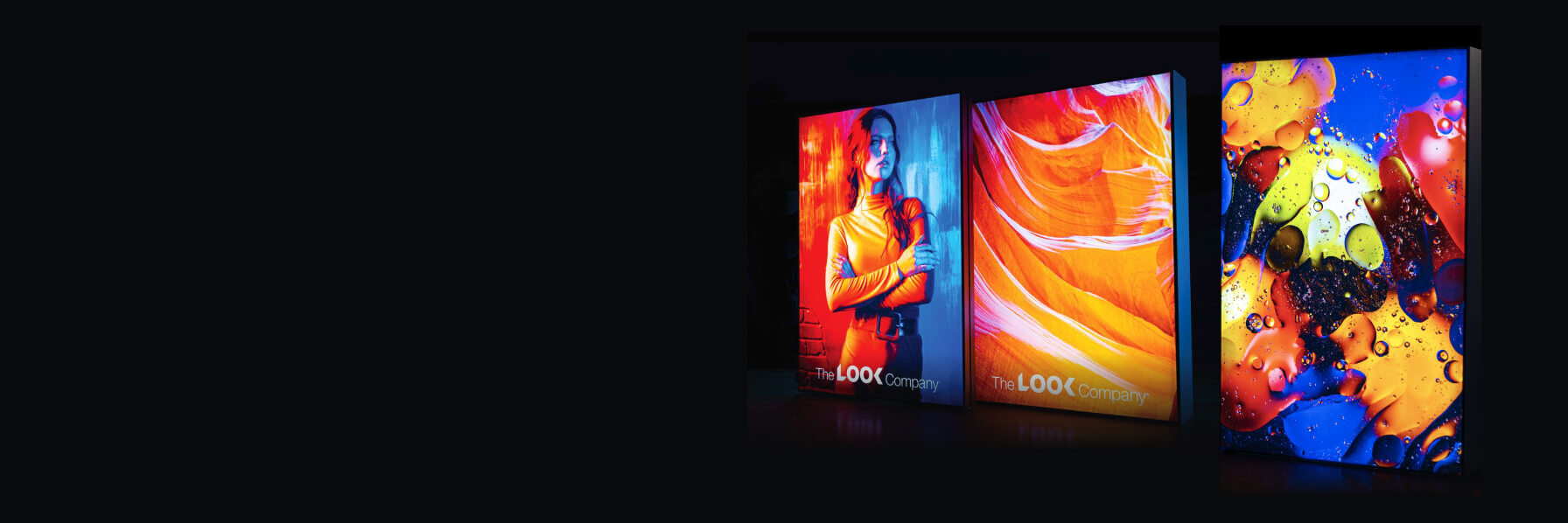 Three vibrant backlit displays showcase a woman in red/blue light, an abstract orange pattern, and colorful oil drops, all branded with ""The LOOK Company"" logo.