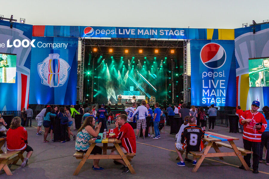 An outdoor concert at the Pepsi Live Main Stage features a band performing, large screens displaying the show, and a crowd gathered with World Cup of Hockey 2016 branding visible.