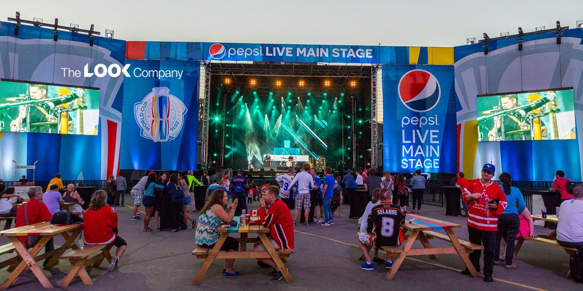 An outdoor concert at the Pepsi Live Main Stage features a band performing, large screens displaying the show, and a crowd gathered with World Cup of Hockey 2016 brand activation.