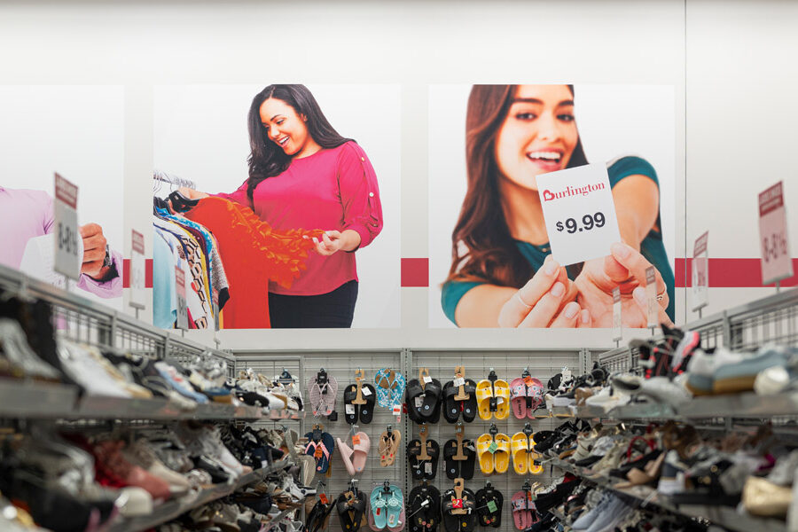 Burlington store interior with shelves of shoes and slippers below large wall graphics of diverse shoppers.