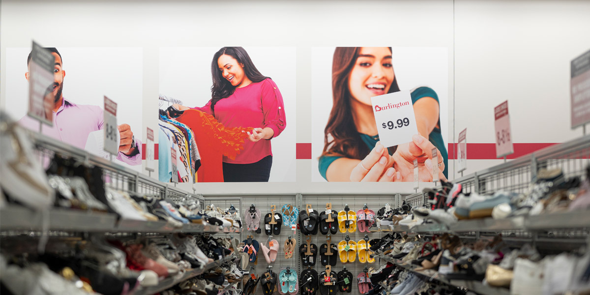Burlington store interior with shelves of shoes and slippers below large wall graphics of diverse shoppers.