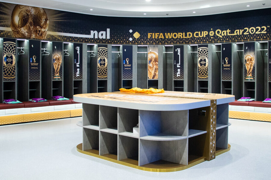 An empty, branded FIFA World Cup Qatar 2022 locker room with individual stalls, player benches, and a central table.