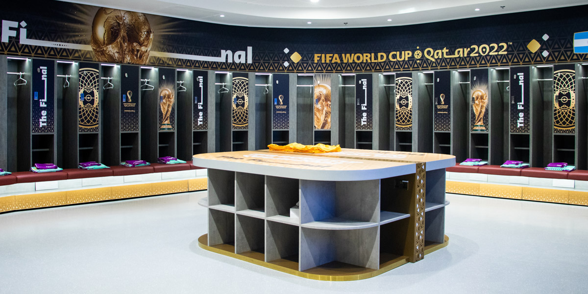 An empty, branded FIFA World Cup Qatar 2022 locker room with individual stalls, player benches, and a central table.