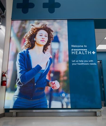 A large in-store banner for Shoppers Health+ features a woman jogging and text promoting their healthcare services.