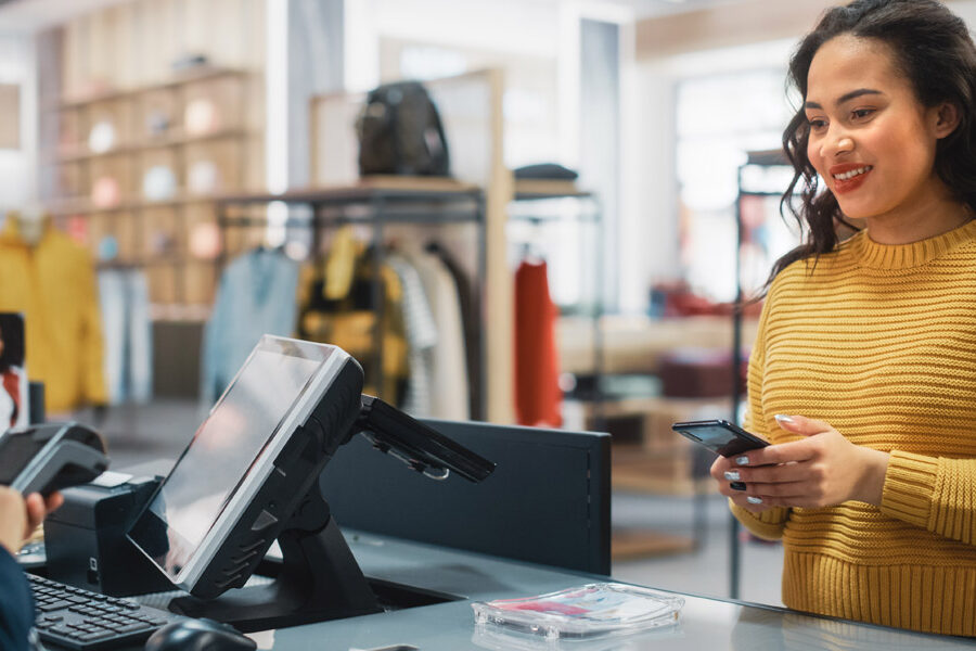 A smiling woman uses her smartphone to pay at a retail checkout counter.