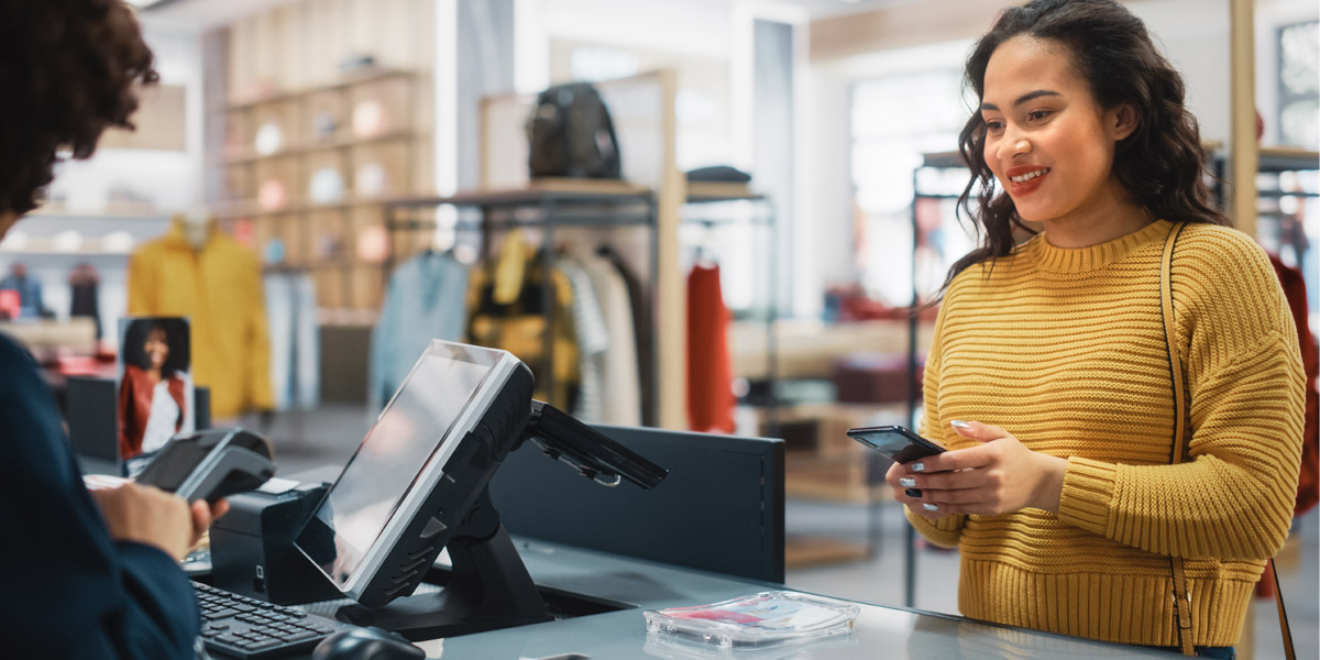 A smiling woman uses her smartphone to pay at a retail checkout counter.