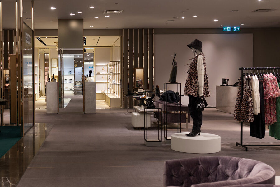 A contemporary luxury department store interior featuring clothing racks, mannequins, and shoe displays under soft lighting.