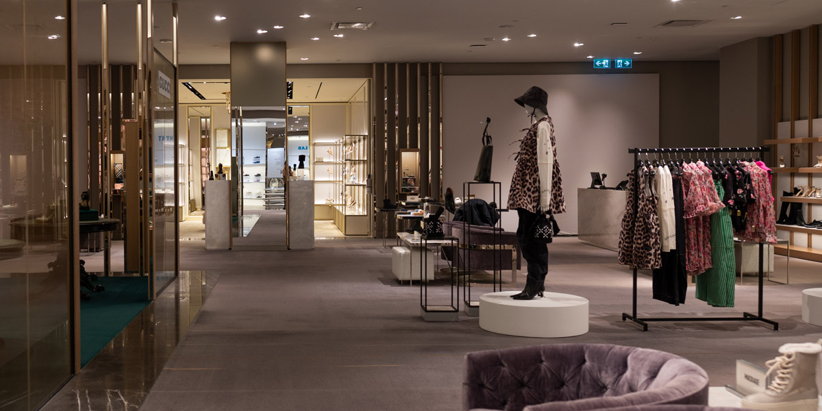 A contemporary luxury department store interior featuring clothing racks, mannequins, and shoe displays under soft lighting.
