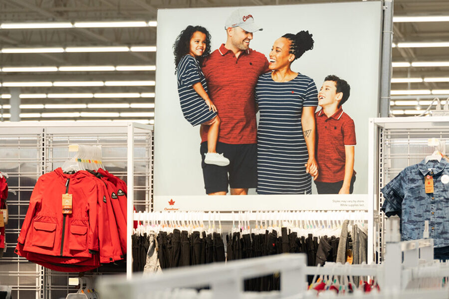 In a clothing store, a large poster shows a smiling family standing above racks of children's clothes.