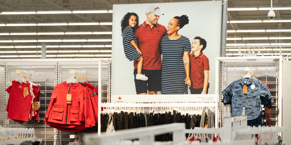 In a clothing store, a large poster shows a smiling family standing above racks of children's clothes.